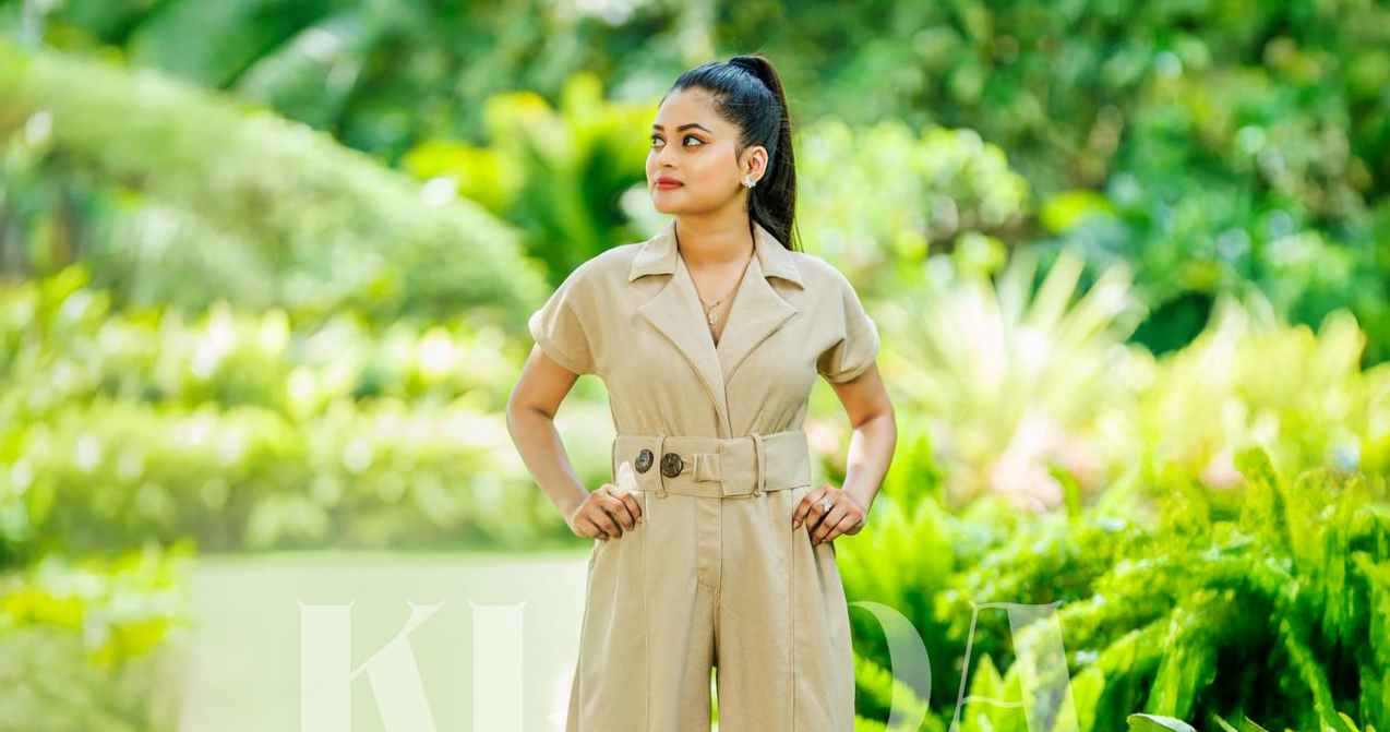 Woman in a beige jumpsuit standing in a lush green garden